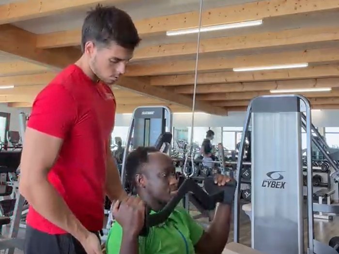 Nicolau Roque, infirmier et personal trainer, corrige la position d'un client sur une machine guidée dans une salle Let's Go Fitness en Valais